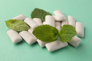 Tasty white chewing gums and mint leaves on turquoise background, closeup