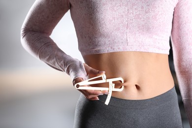 Photo of Woman measuring body fat layer with caliper indoors, closeup