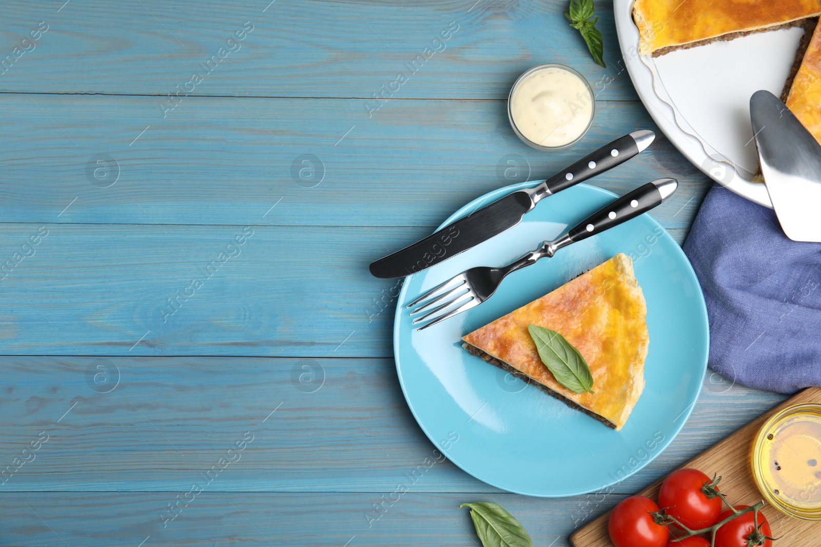 Photo of Piece of delicious pie with minced meat and basil served on light blue wooden table, flat lay. Space for text