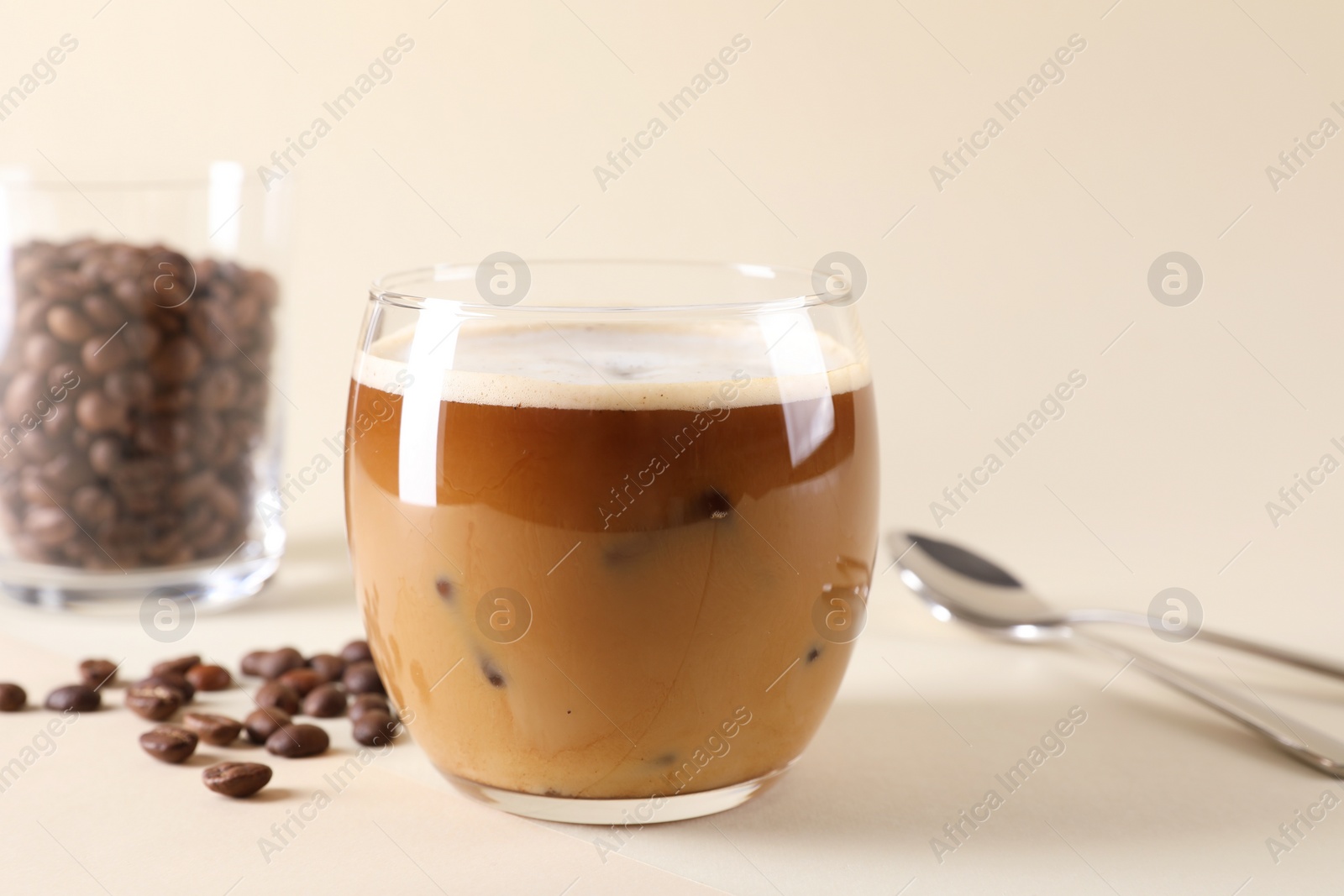 Photo of Refreshing iced coffee with milk in glass and beans on beige background