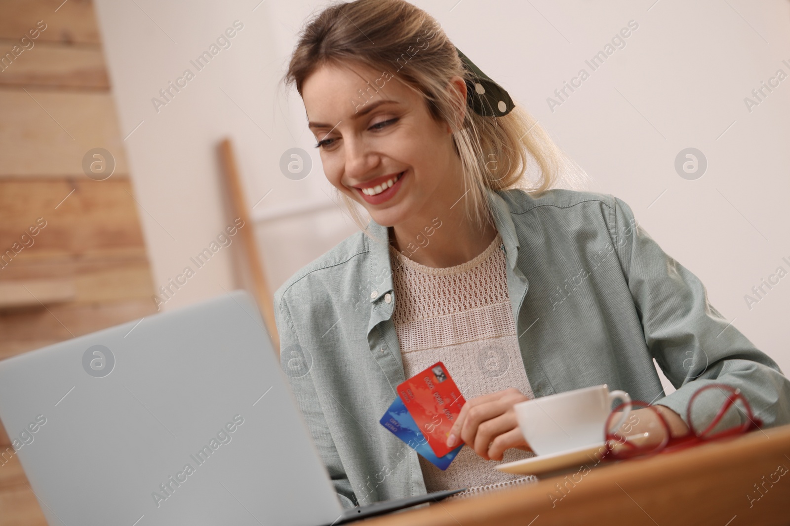 Photo of Woman with credit cards using laptop for online shopping at wooden table indoors