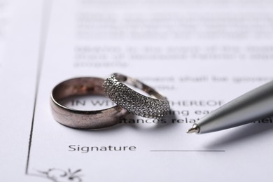 Photo of Marriage contract, pen and wedding rings, closeup