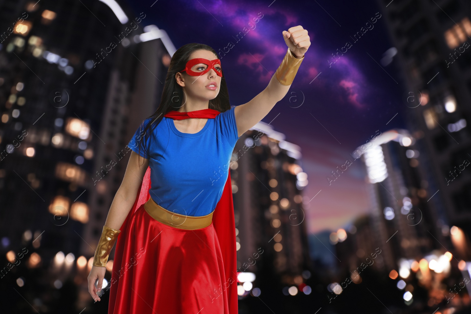 Image of Confident young woman wearing superhero costume and beautiful cityscape in night on background