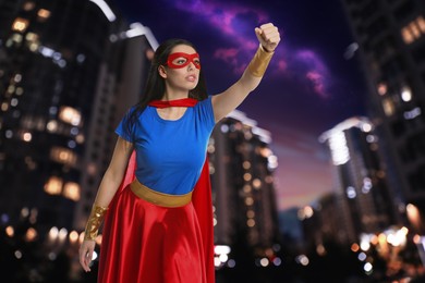 Image of Confident young woman wearing superhero costume and beautiful cityscape in night on background