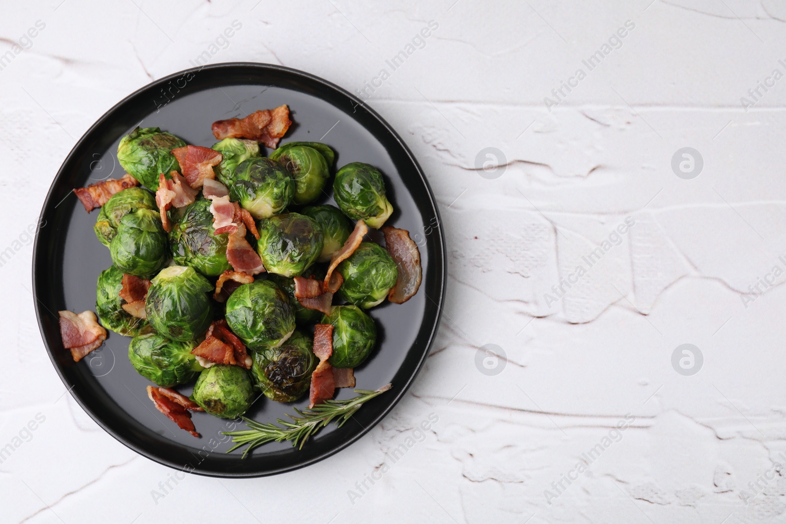 Photo of Delicious roasted Brussels sprouts, bacon and rosemary on white textured table, top view. Space for text