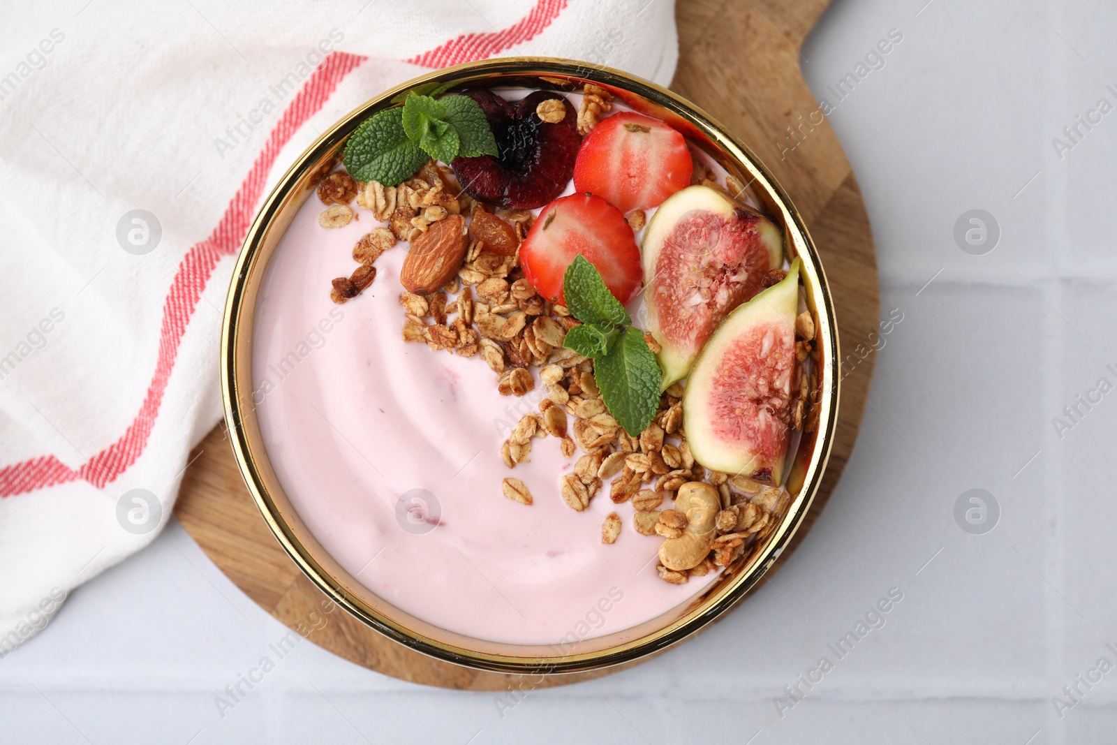 Photo of Bowl with yogurt, fruits and granola on white tiled table, top view