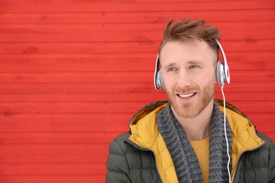 Young man listening to music with headphones against color wall. Space for text
