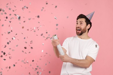 Photo of Emotional man blowing up party popper on pink background