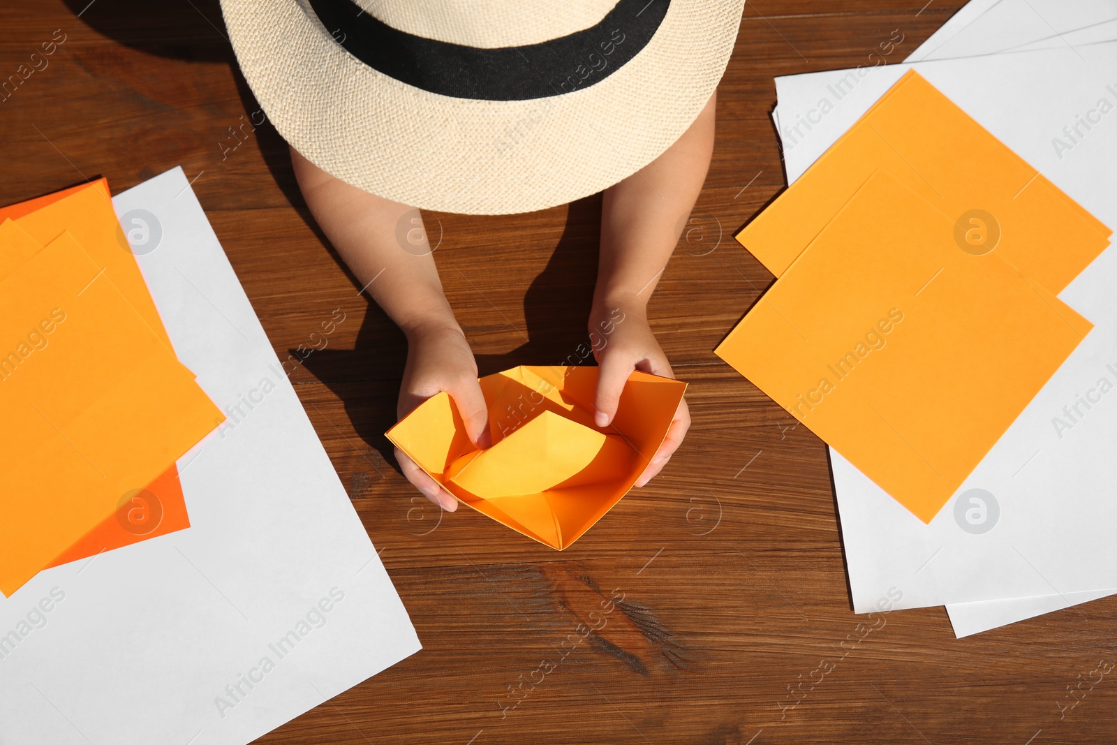 Photo of Little child making paper boat at wooden table, top view