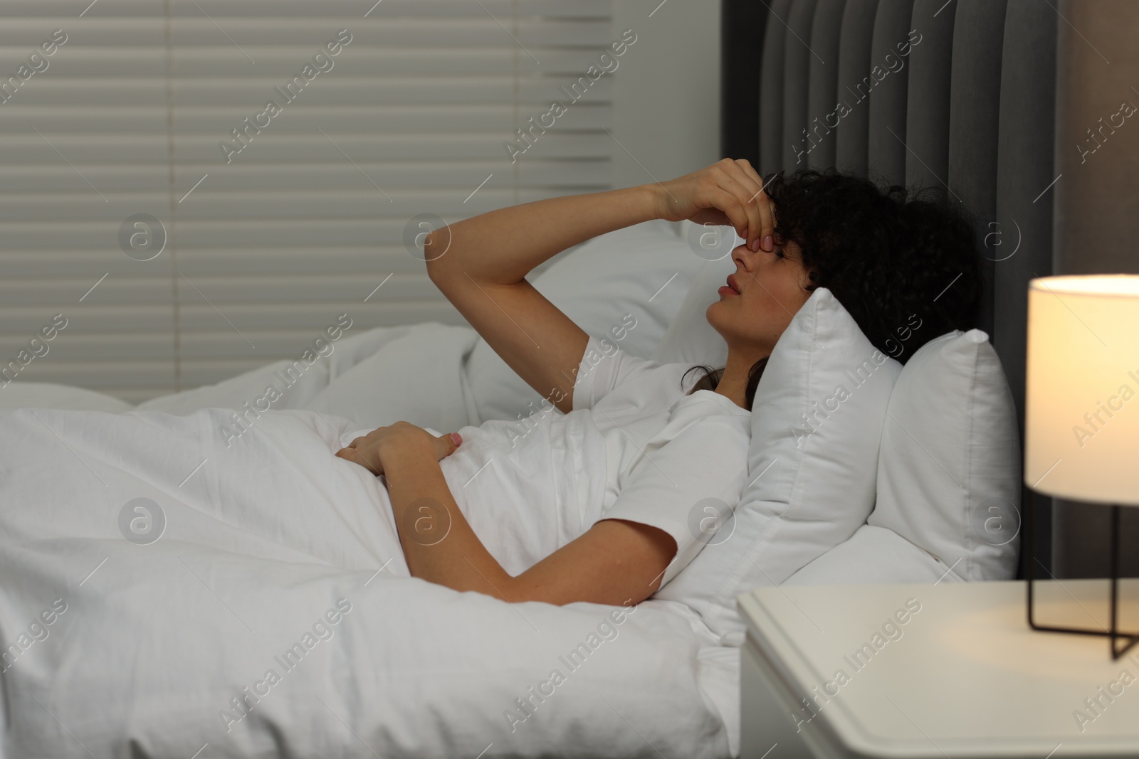 Photo of Young woman suffering from headache in bed at night