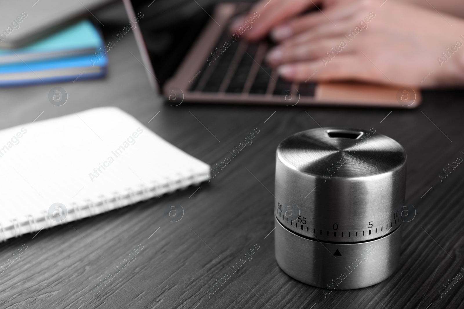 Photo of Woman working on laptop at wooden table, focus on kitchen timer. Space for text