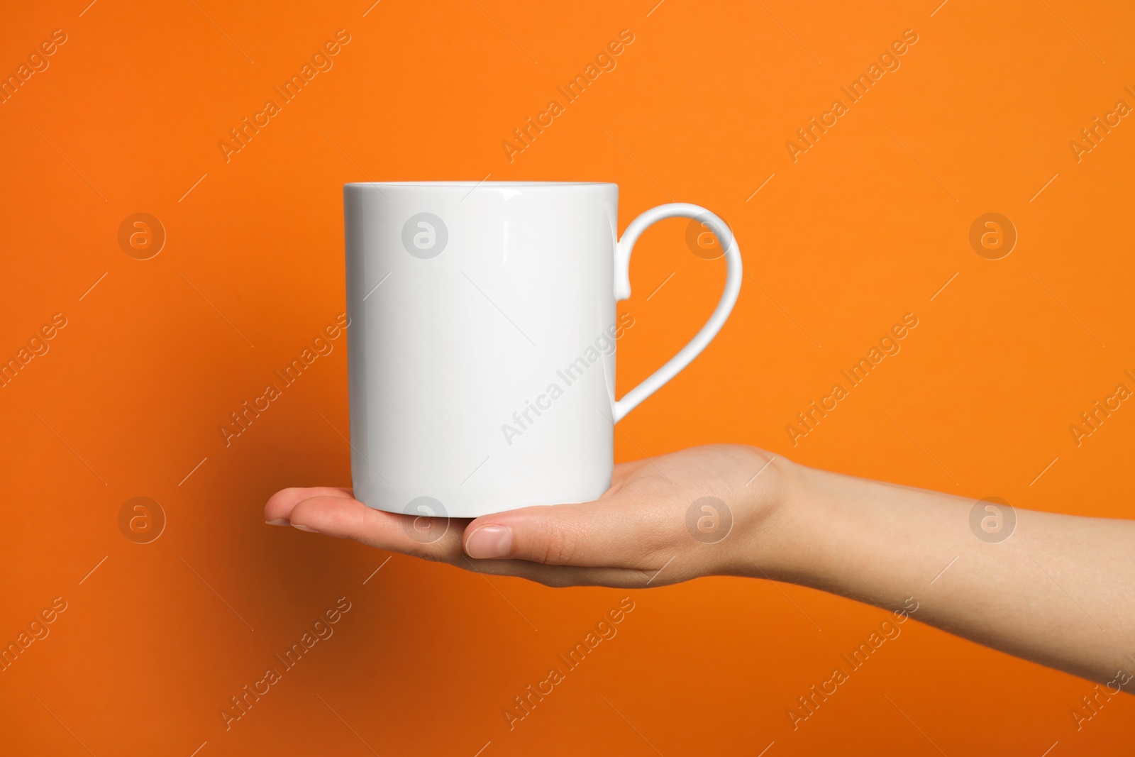 Photo of Woman holding white mug on orange background, closeup