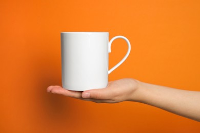 Photo of Woman holding white mug on orange background, closeup