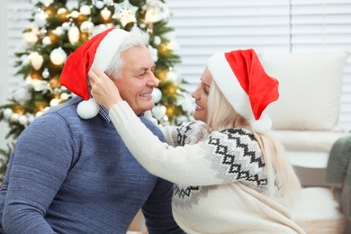 Happy mature couple in Santa hats at home. Christmas celebration