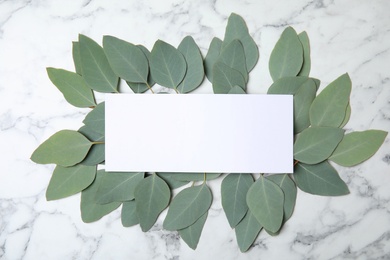 Photo of Fresh eucalyptus leaves and blank card with space for design on marble background, top view