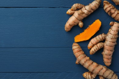 Whole and cut turmeric roots on blue wooden table, flat lay. Space for text