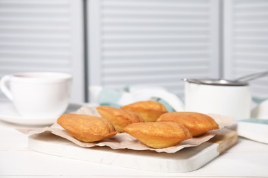 Tasty madeleine cookies and cup of tea on white wooden table