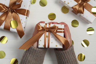 Photo of Christmas present. Woman with gift boxes and confetti at white wooden table, top view