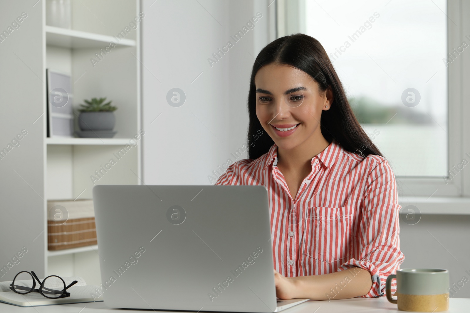 Photo of Young woman working with laptop at workplace in office