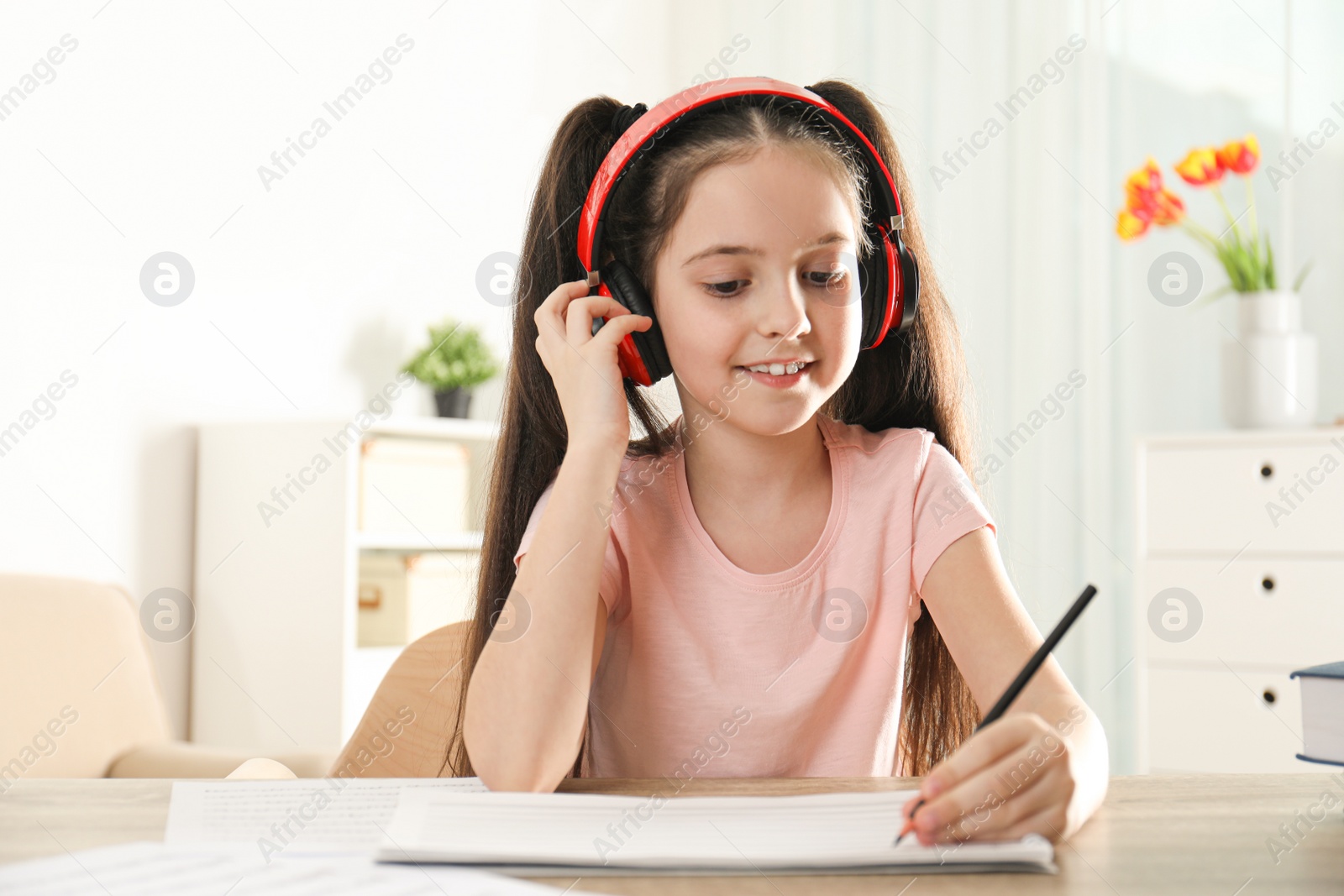 Photo of Little girl writing music notes at table indoors