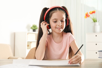 Little girl writing music notes at table indoors