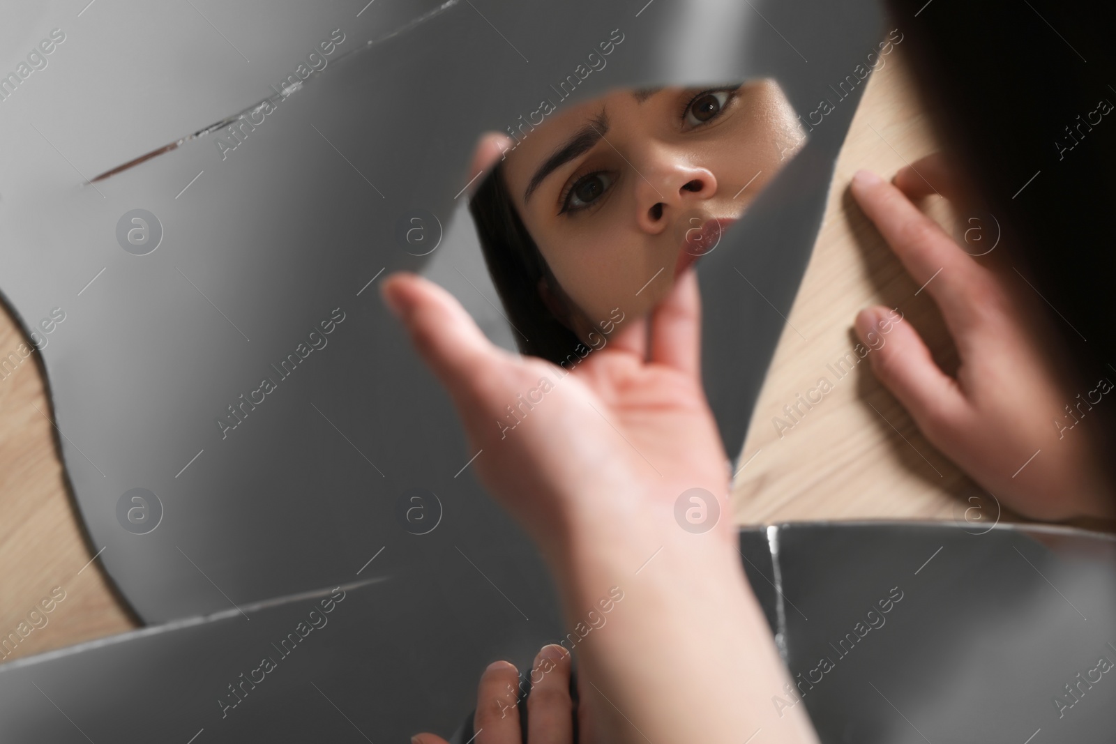 Photo of Young woman looking at herself in shard of broken mirror on background, closeup