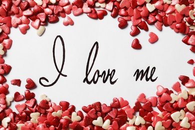 Photo of Handwritten phrase I Love Me and heart shaped sprinkles on white background, flat lay