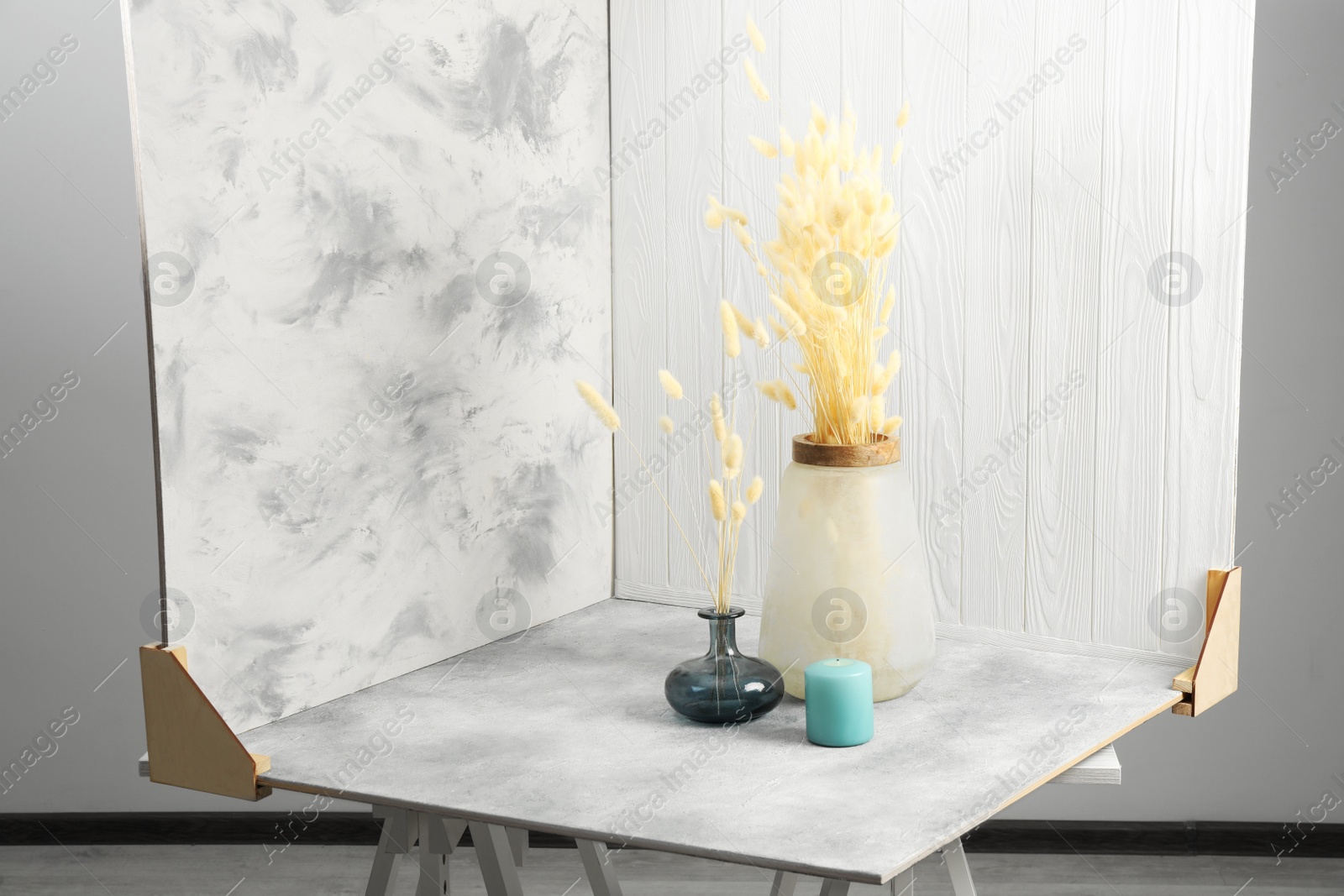 Photo of Vases with beautiful dry flowers, candle and double-sided backdrops on table in photo studio