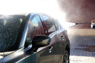 Photo of Worker cleaning automobile with high pressure water jet at car wash