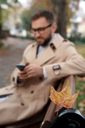 Photo of Handsome man wearing stylish clothes in autumn park, focus on yellow leaf