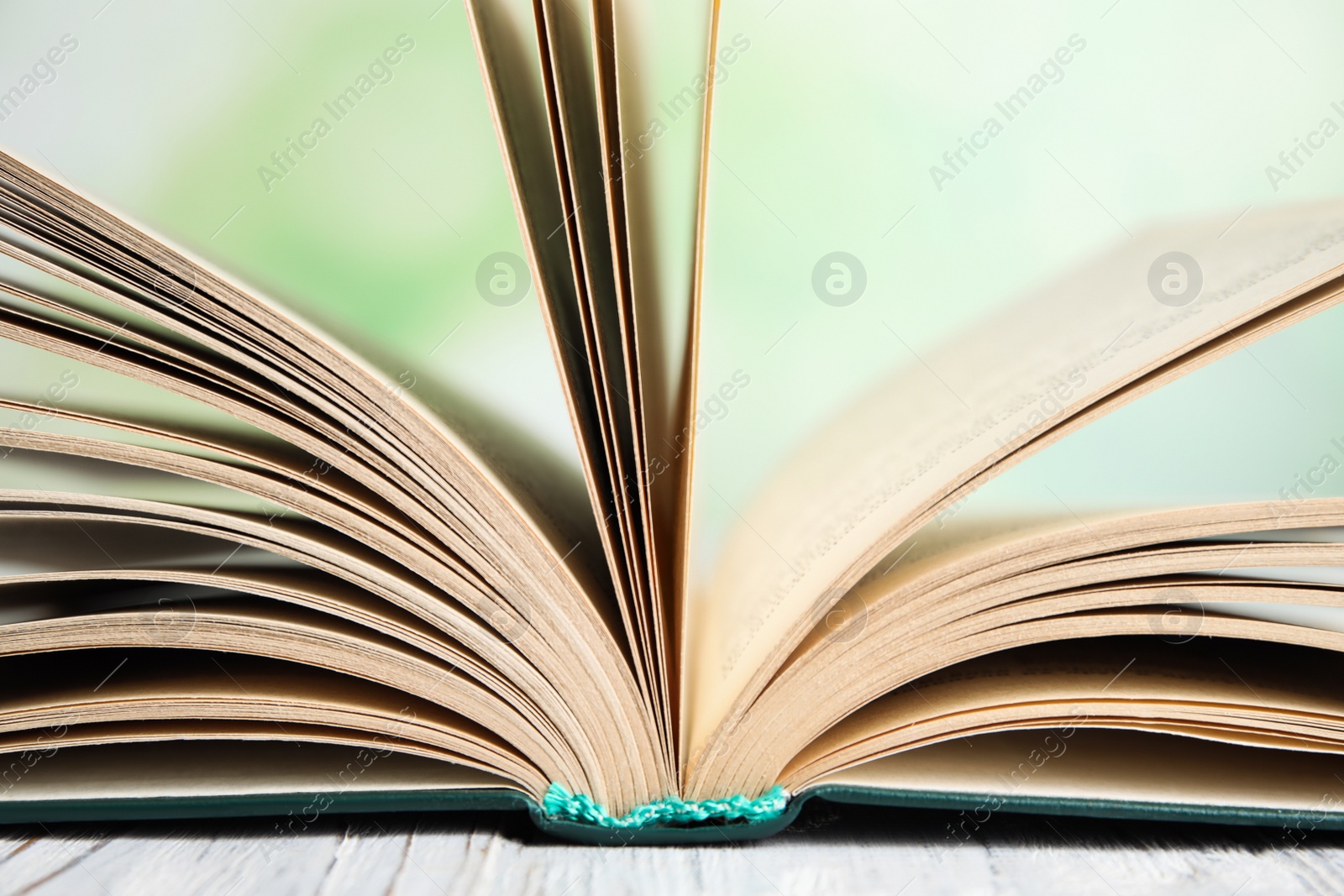 Photo of Open book on white wooden table against blurred green background, closeup