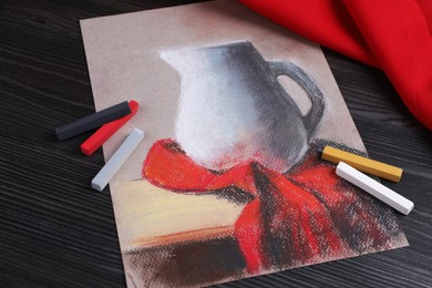 Photo of Colorful chalk pastels and beautiful painting of jug on black wooden table