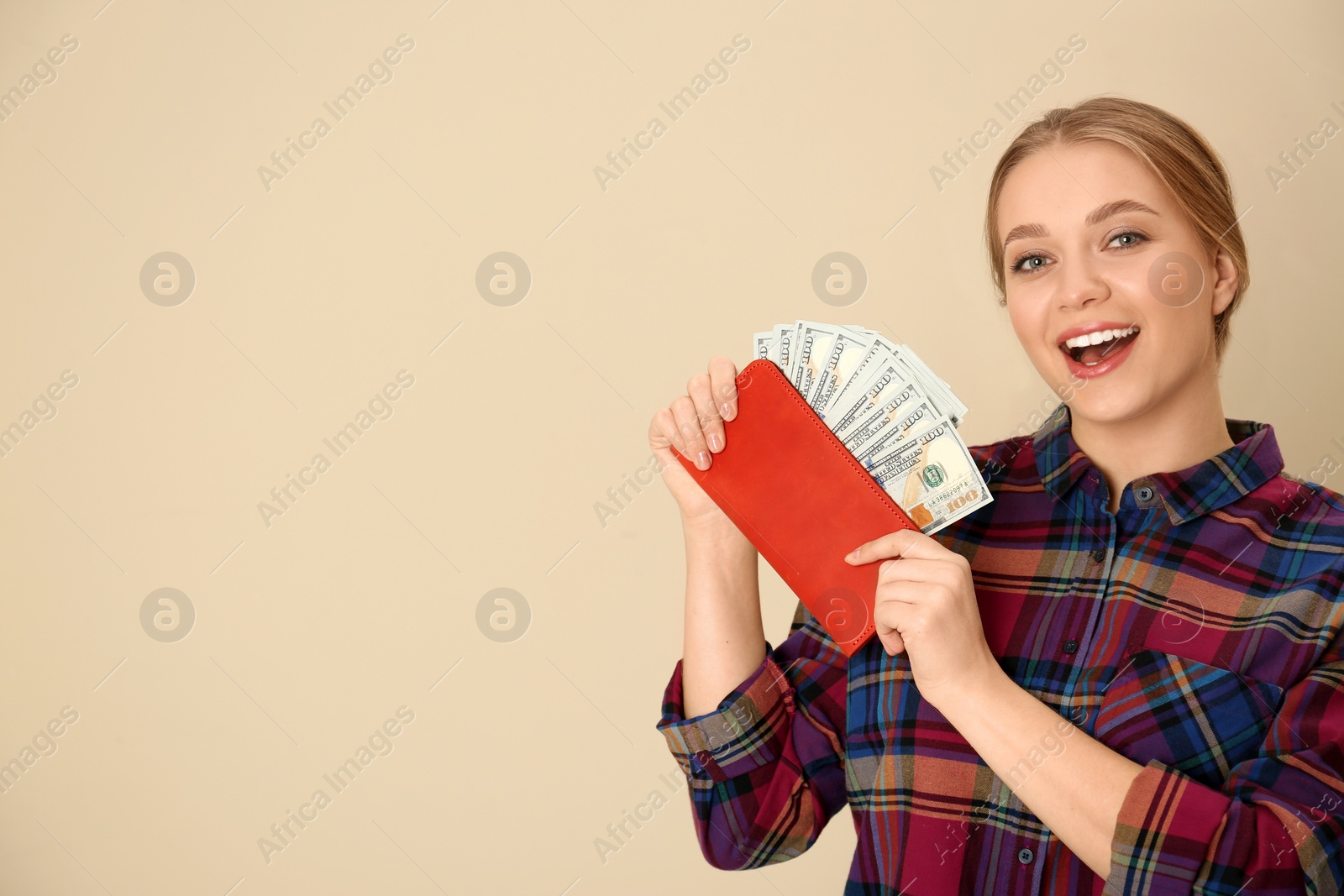 Photo of Happy young woman with wallet full of money on color background. Space for text