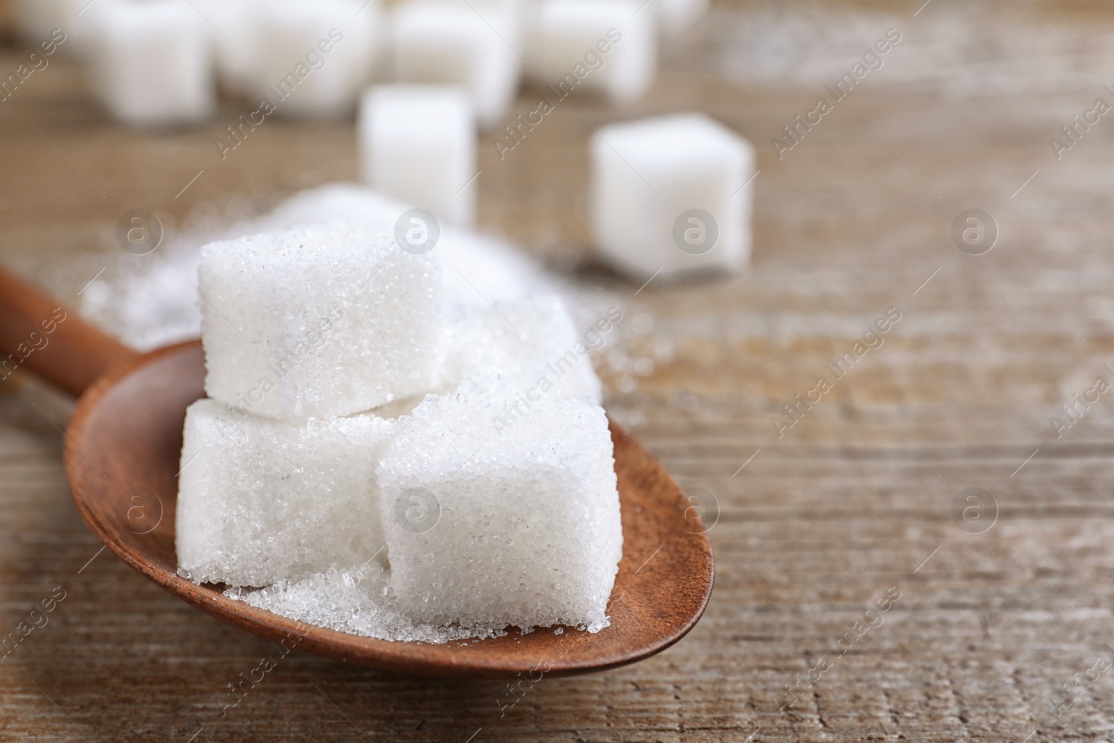 Photo of Refined sugar in spoon on wooden table, closeup. Space for text