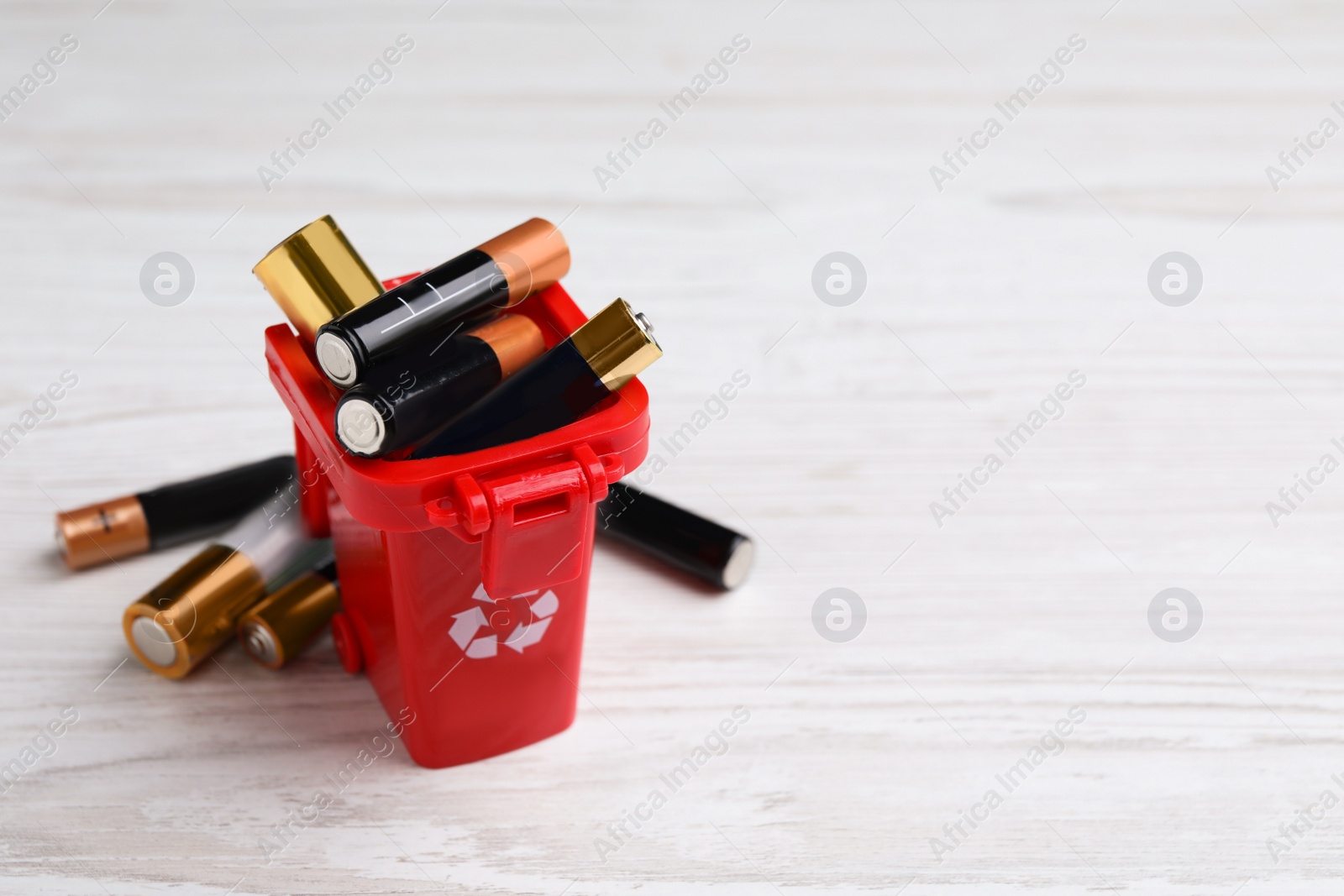 Image of Used batteries and recycling bin on white wooden table, space for text