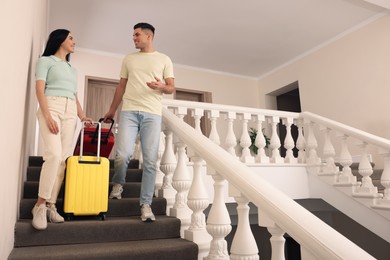 Photo of Happy couple with suitcases going down stairs in hotel