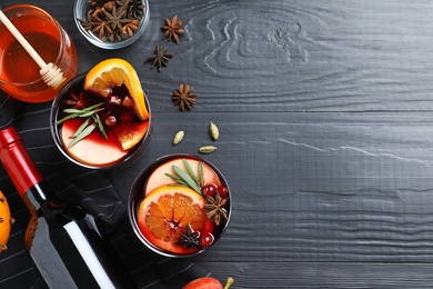 Photo of Cups of tasty mulled wine on black wooden table, flat lay. Space for text