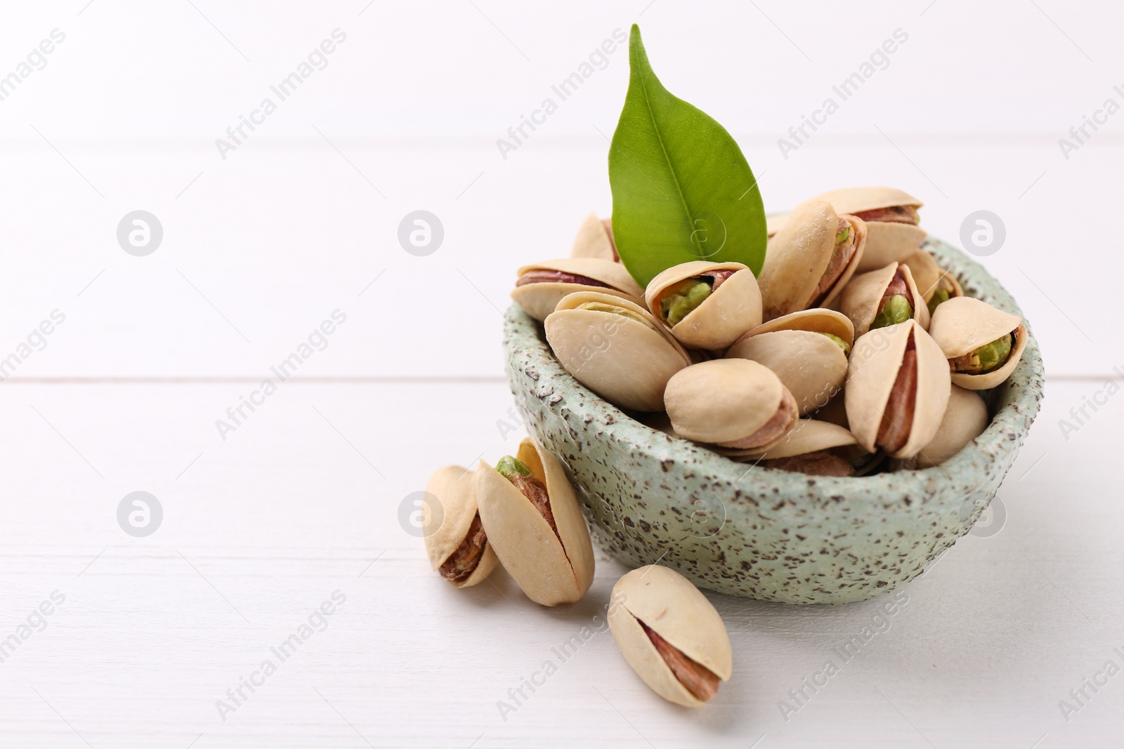 Photo of Delicious pistachios in bowl on white table. Space for text