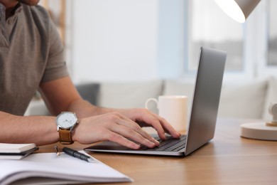 Man working on laptop at wooden desk indoors, closeup