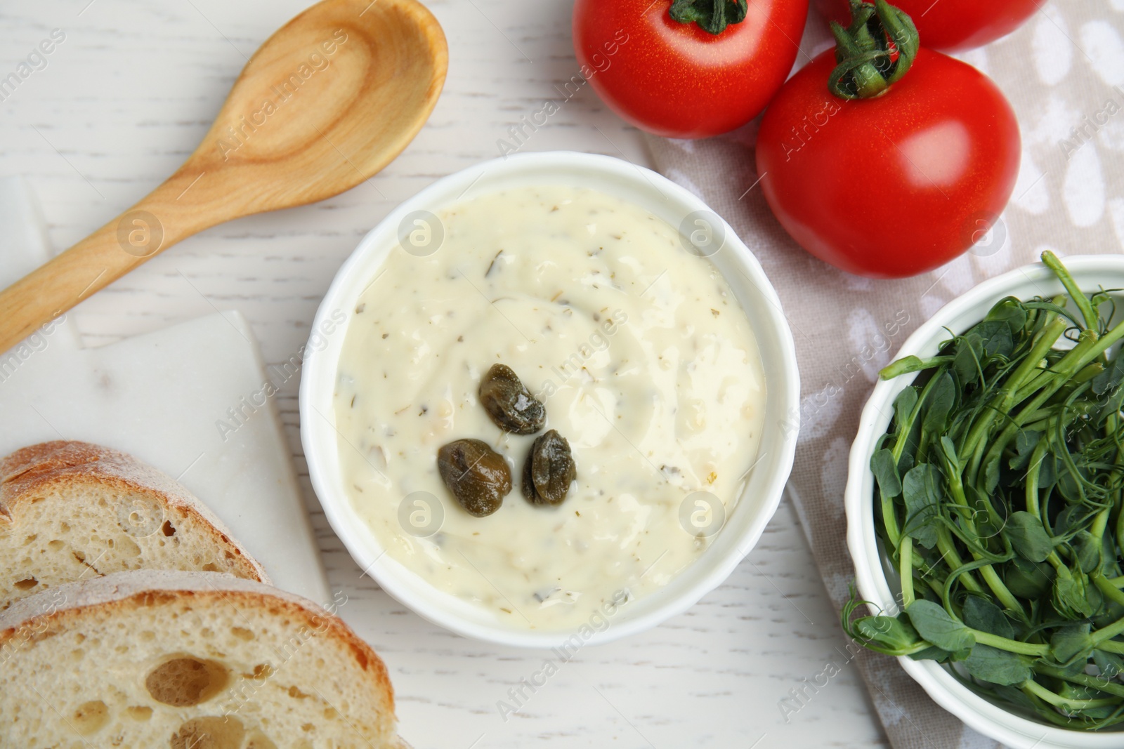 Photo of Creamy caper sauce in bowl on white wooden table, flat lay