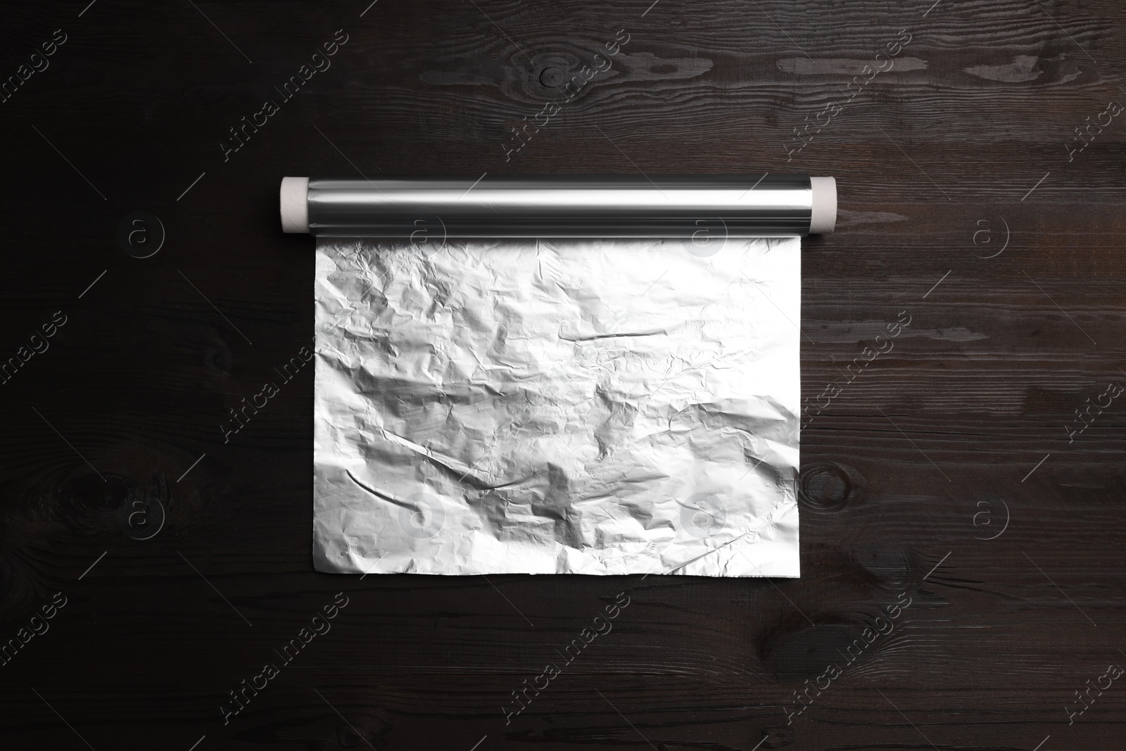 Photo of Roll of aluminum foil on dark wooden table, top view