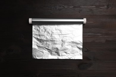 Roll of aluminum foil on dark wooden table, top view