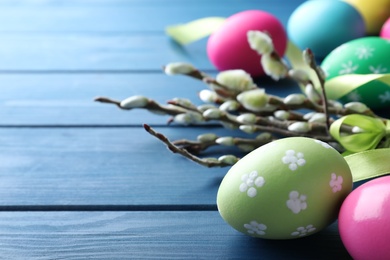 Photo of Bright painted eggs and pussy willows on blue wooden table, closeup view with space for text. Happy Easter