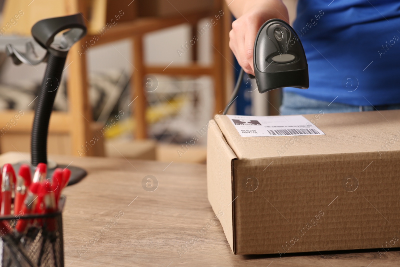 Photo of Post office worker with scanner reading parcel barcode at counter, closeup