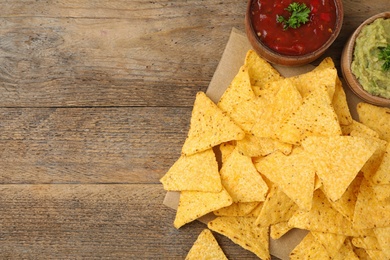 Photo of Mexican nacho chips with different sauces on wooden background, flat lay. Space for text