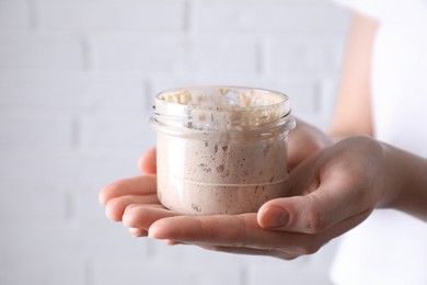 Woman holding glass jar with fresh sourdough starter on blurred background, closeup. Space for text