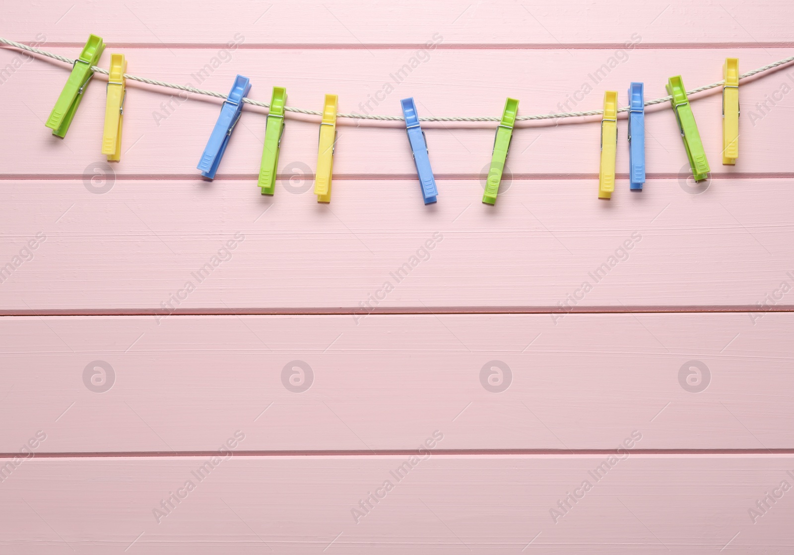 Photo of Colorful plastic clothespins and rope on pink wooden background. Space for text