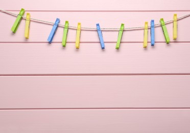 Colorful plastic clothespins and rope on pink wooden background. Space for text