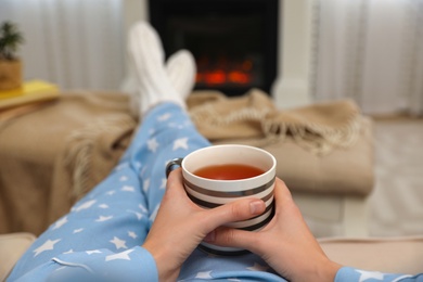 Photo of Woman with cup of tea resting near fireplace at home, closeup