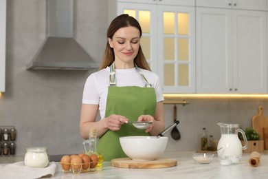 Photo of Making bread. Woman sifting flour onto dough at white table in kitchen